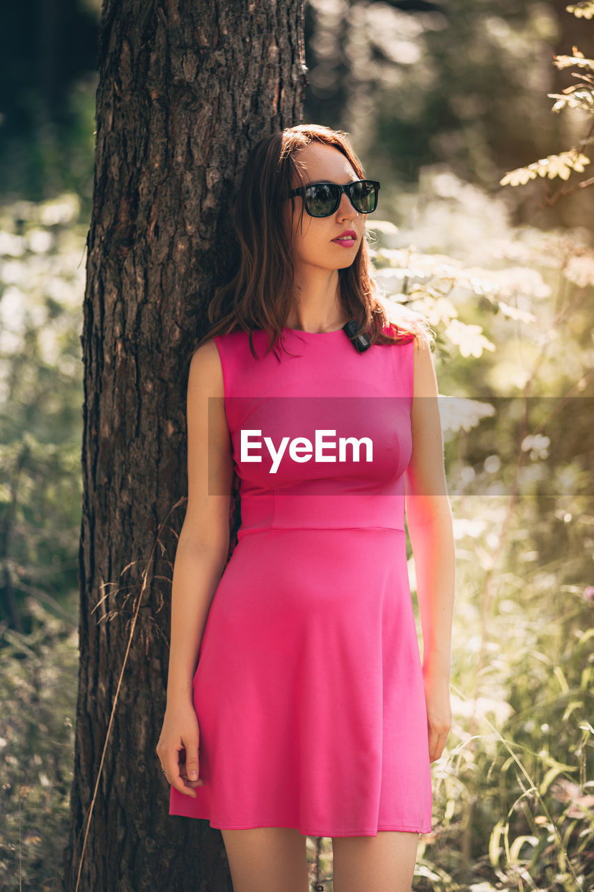 Beautiful woman portrait in sunglasses and pink dress in forest