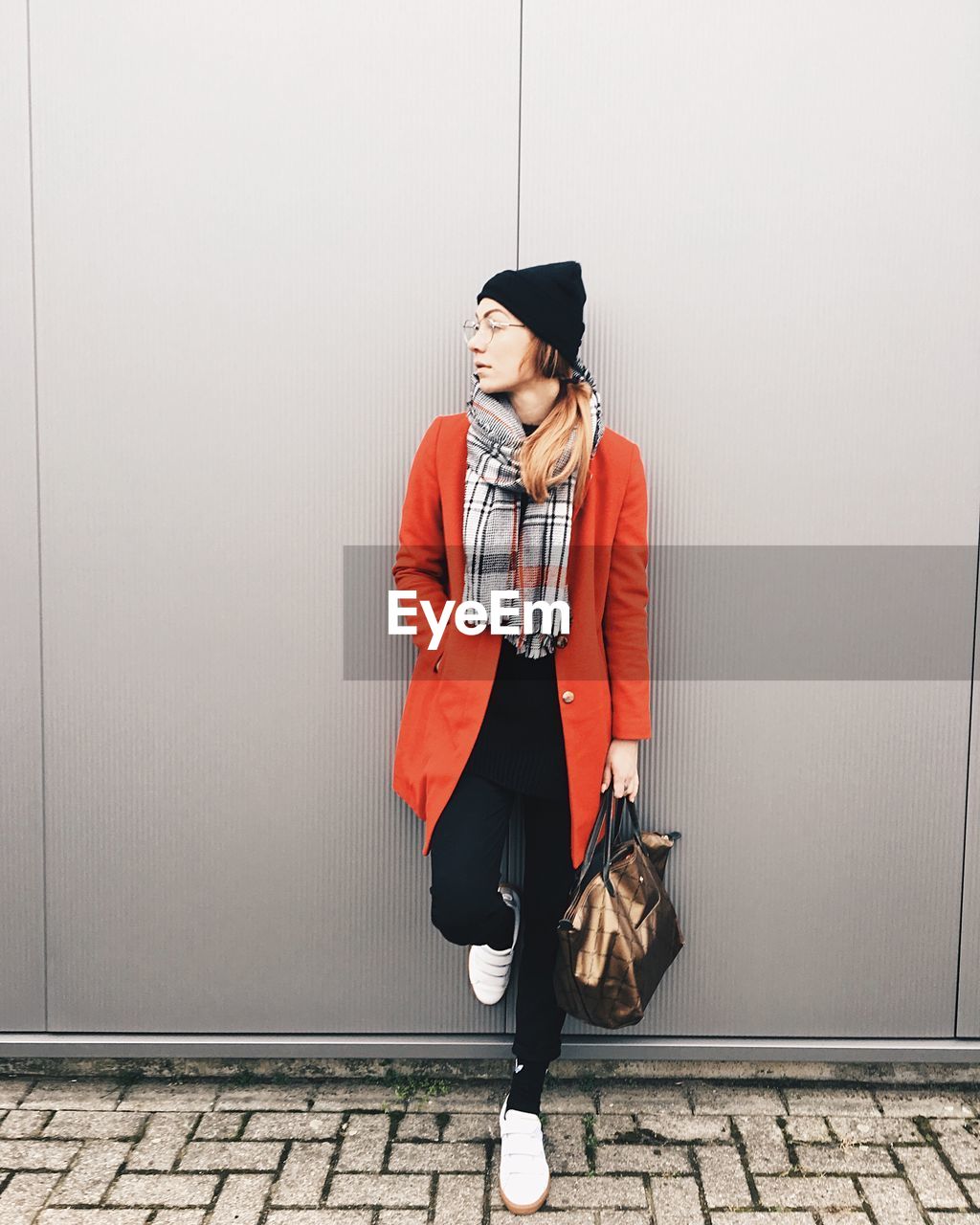 Young woman while standing on footpath against wall