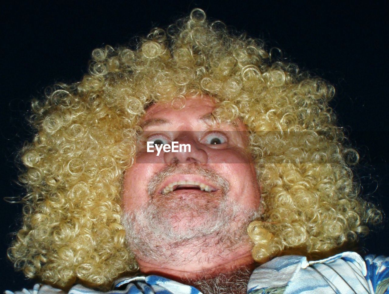 Portrait of mature man wearing blond curly hair wig against black background
