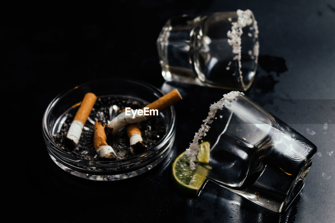 High angle view of shot glasses by cigarette butts on table