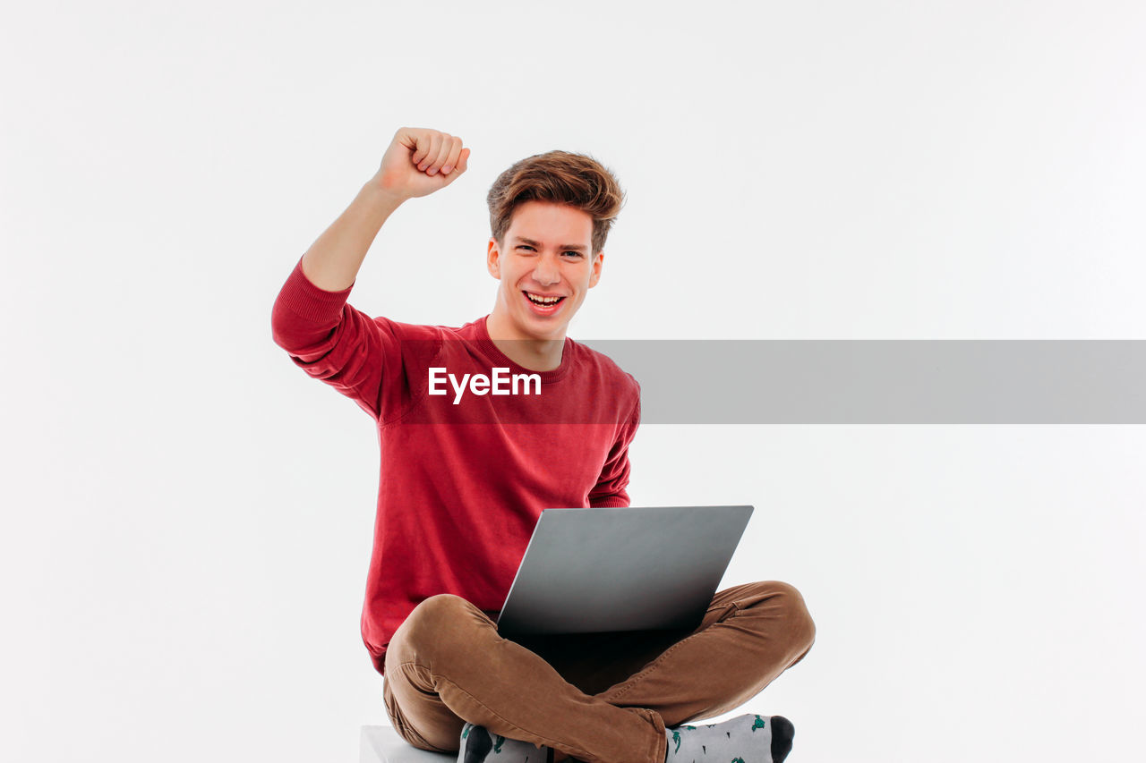 Portrait of young man celebrating success while using laptop against white background