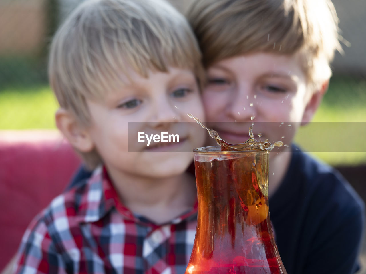 Two caucasian boys watches a splash of tea in a cup from a falling piece of sugar