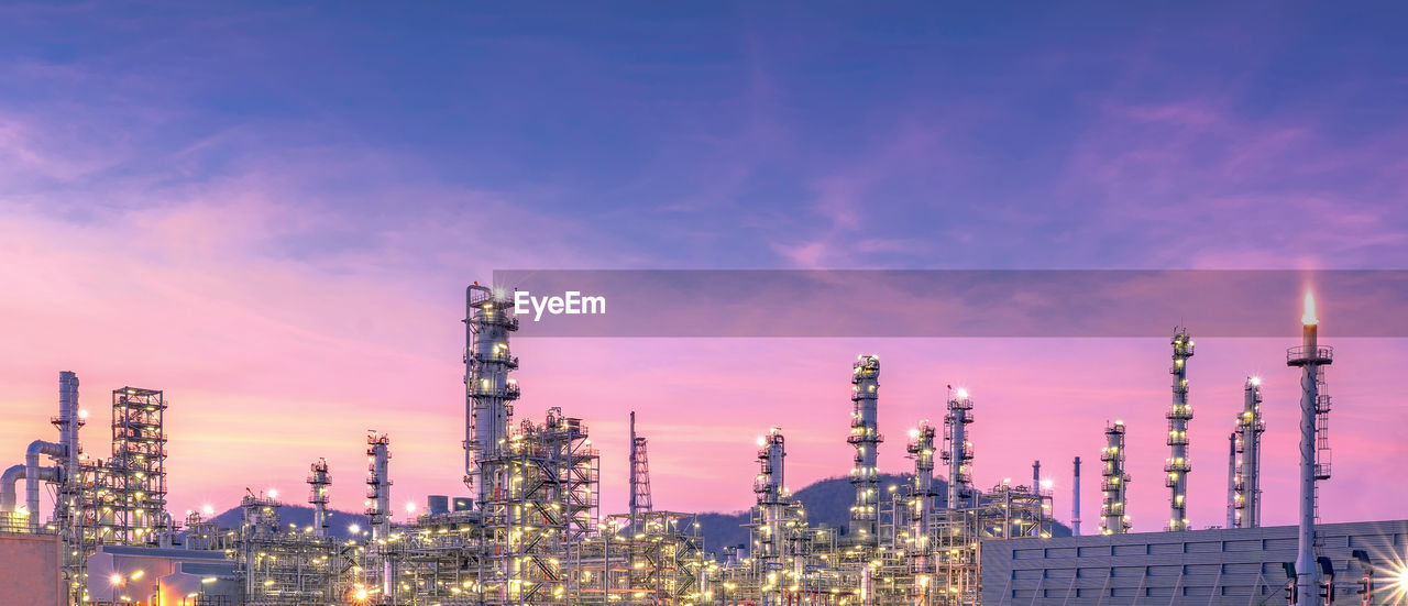 PANORAMIC VIEW OF ILLUMINATED FACTORY AGAINST SKY AT DUSK