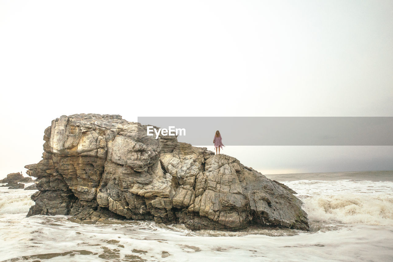 Woman standing on rock formations at beach against clear sky