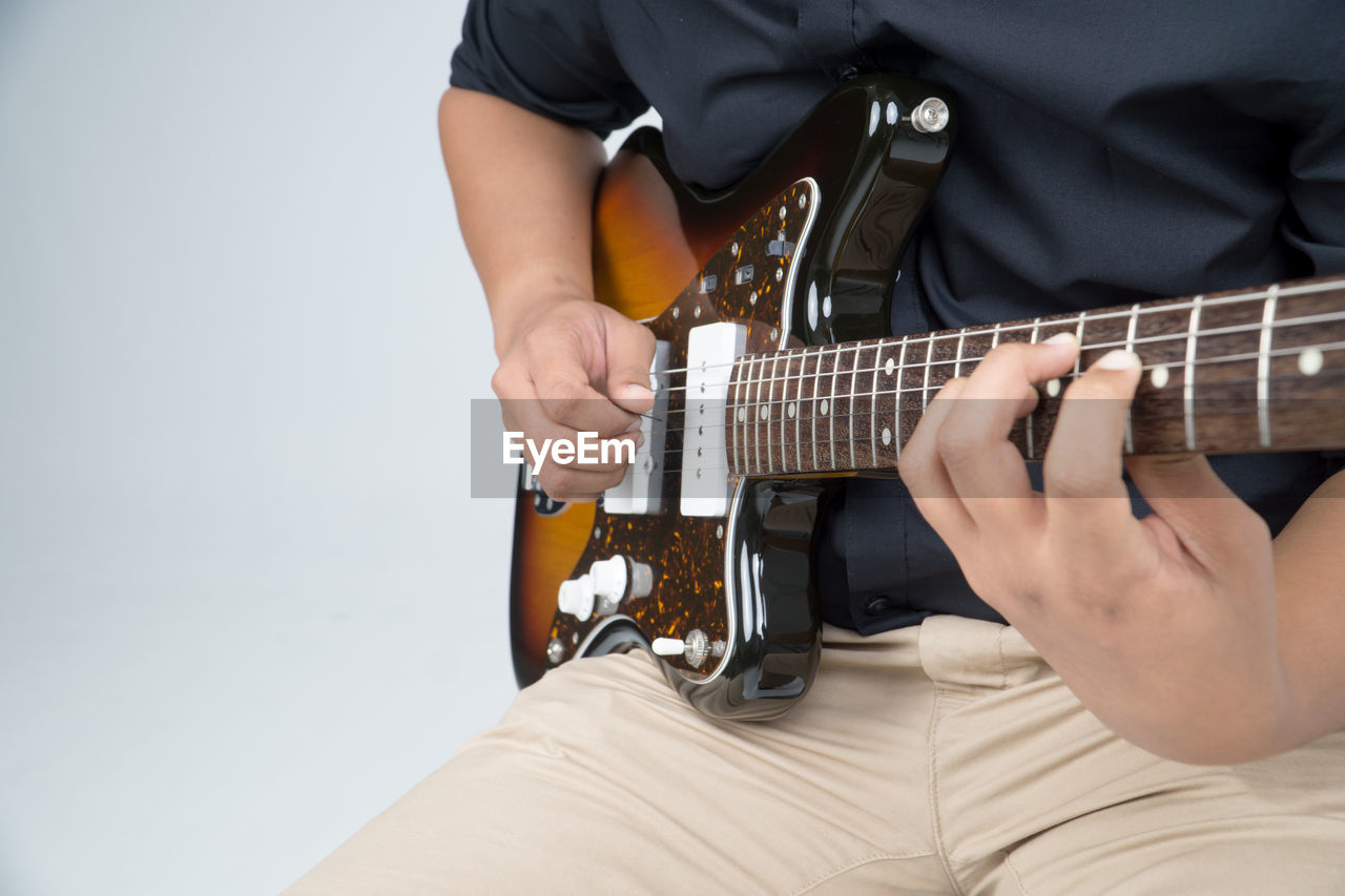 Midsection of musician playing guitar against white background