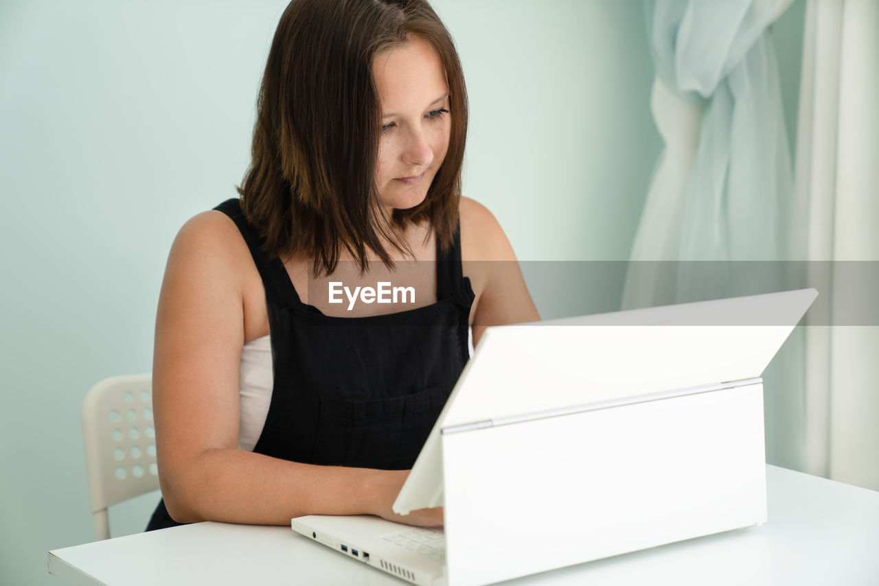 Girl is sitting in front of white laptop transformer at desk. concept of remote work and education