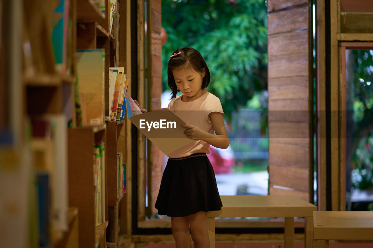 Cute girl reading book while standing at library