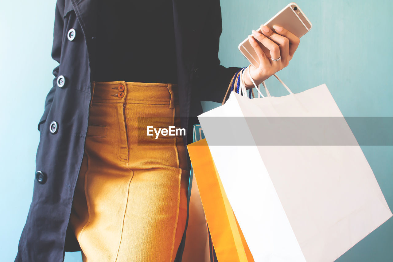 Midsection of woman holding shopping bags and mobile phone