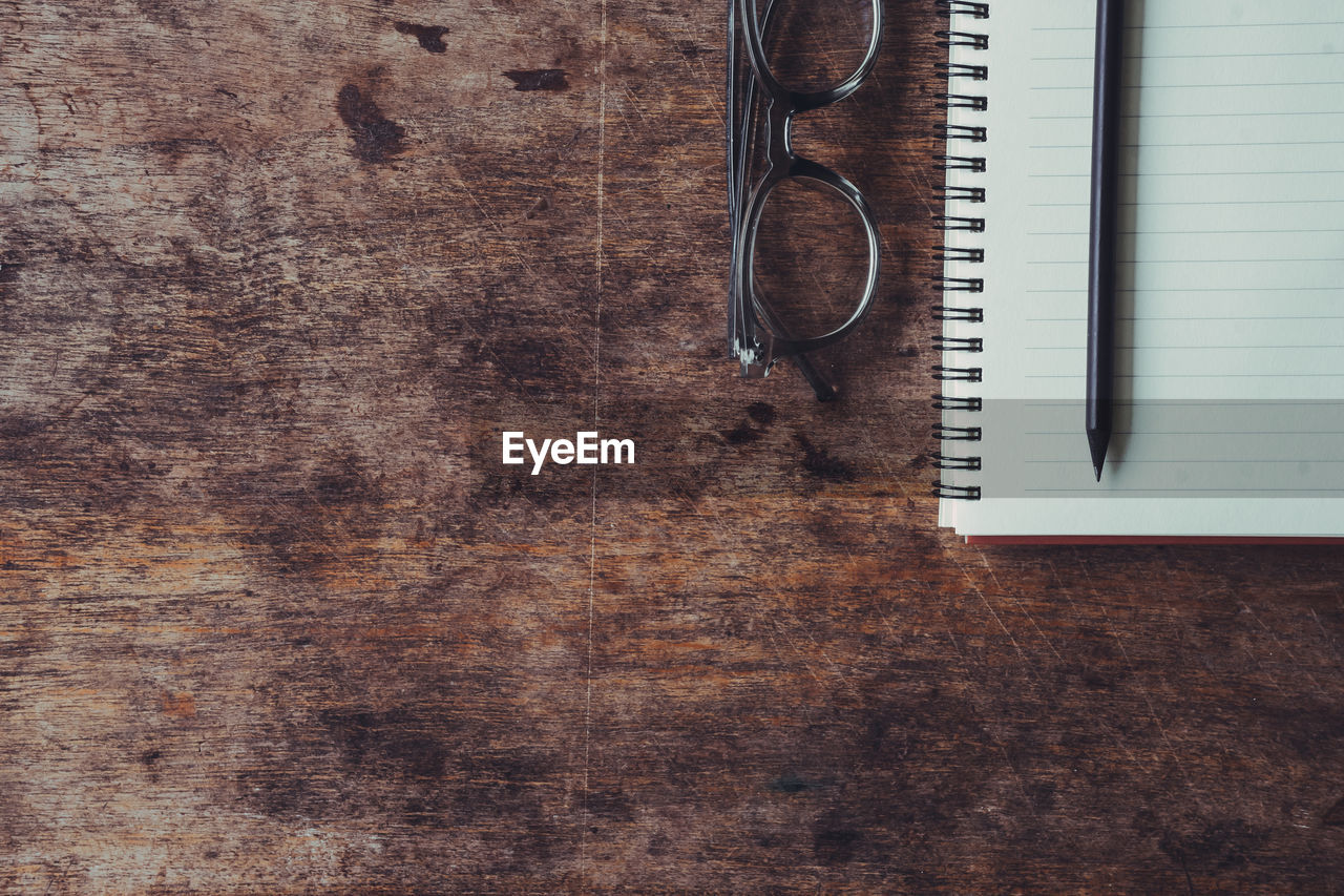 Directly above shot of book with pencils and eyeglasses on wooden table