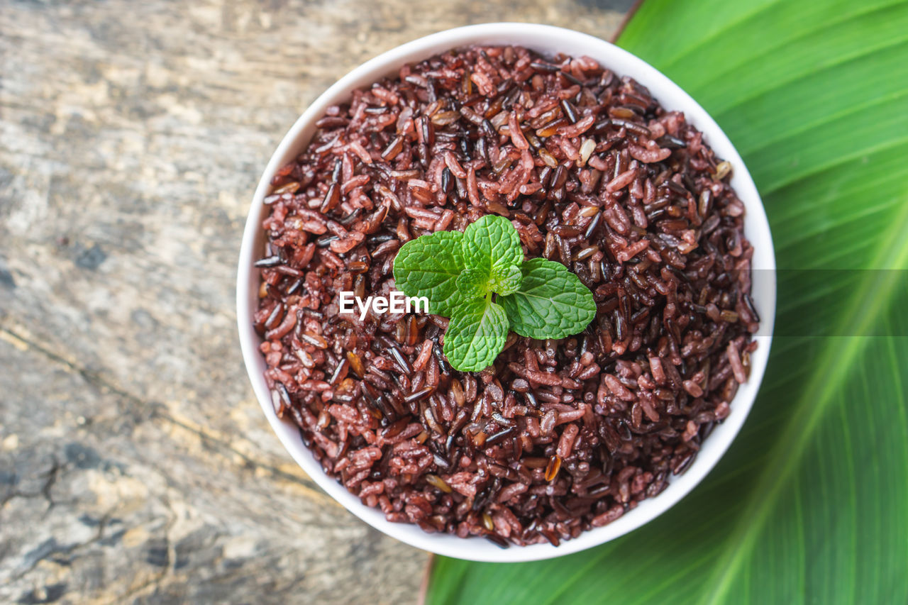 Cooked purple rice berry in bowl over green leaf background on wooden table closeup