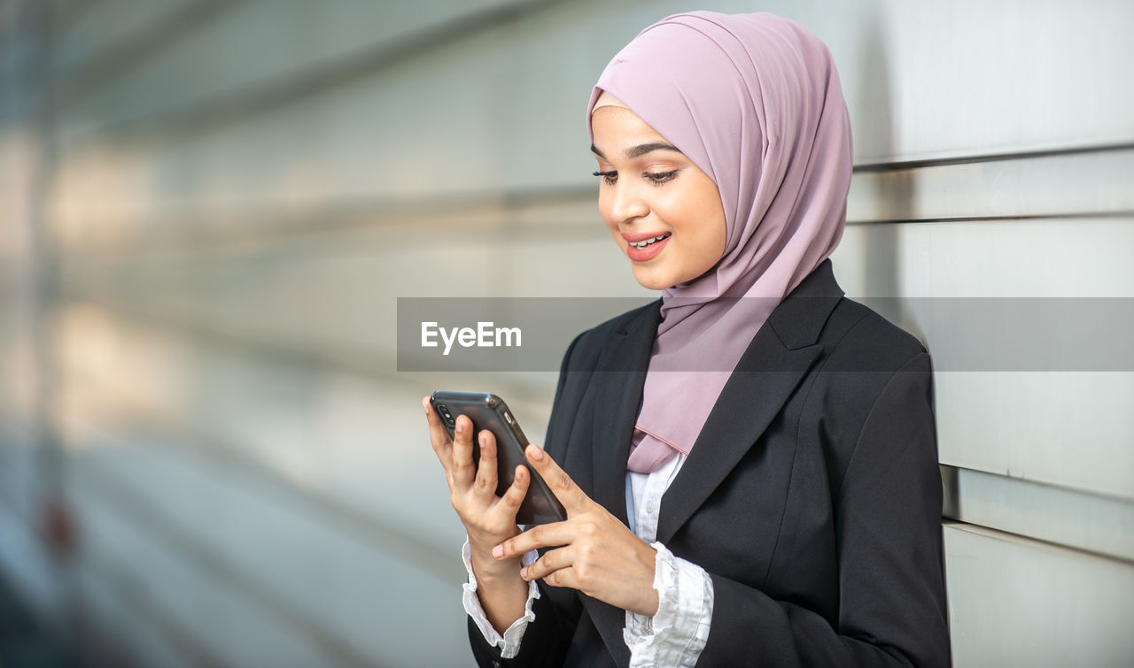 MID ADULT WOMAN USING PHONE WHILE STANDING ON MOBILE