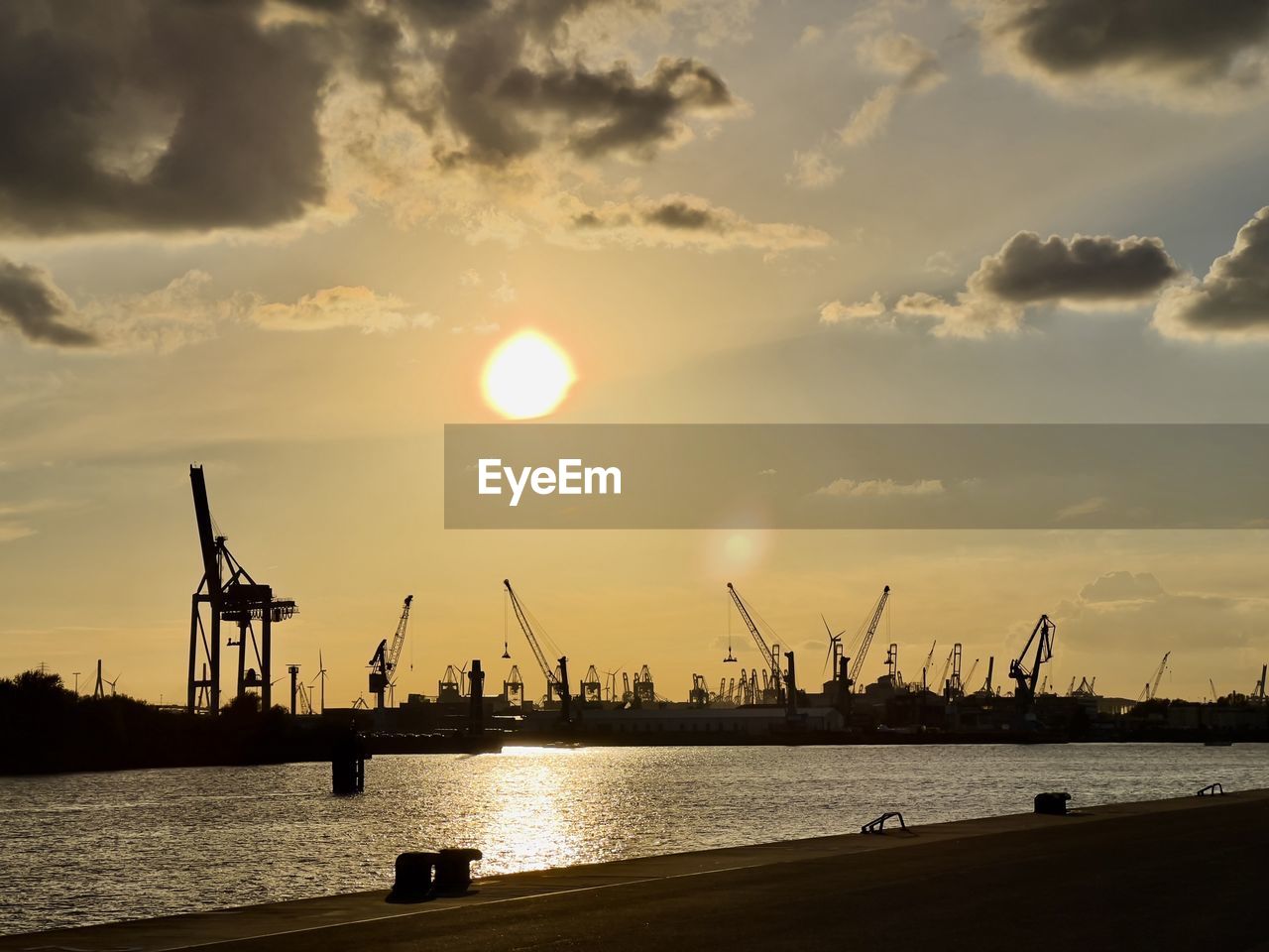 SILHOUETTE CRANES AT HARBOR AGAINST SKY AT SUNSET