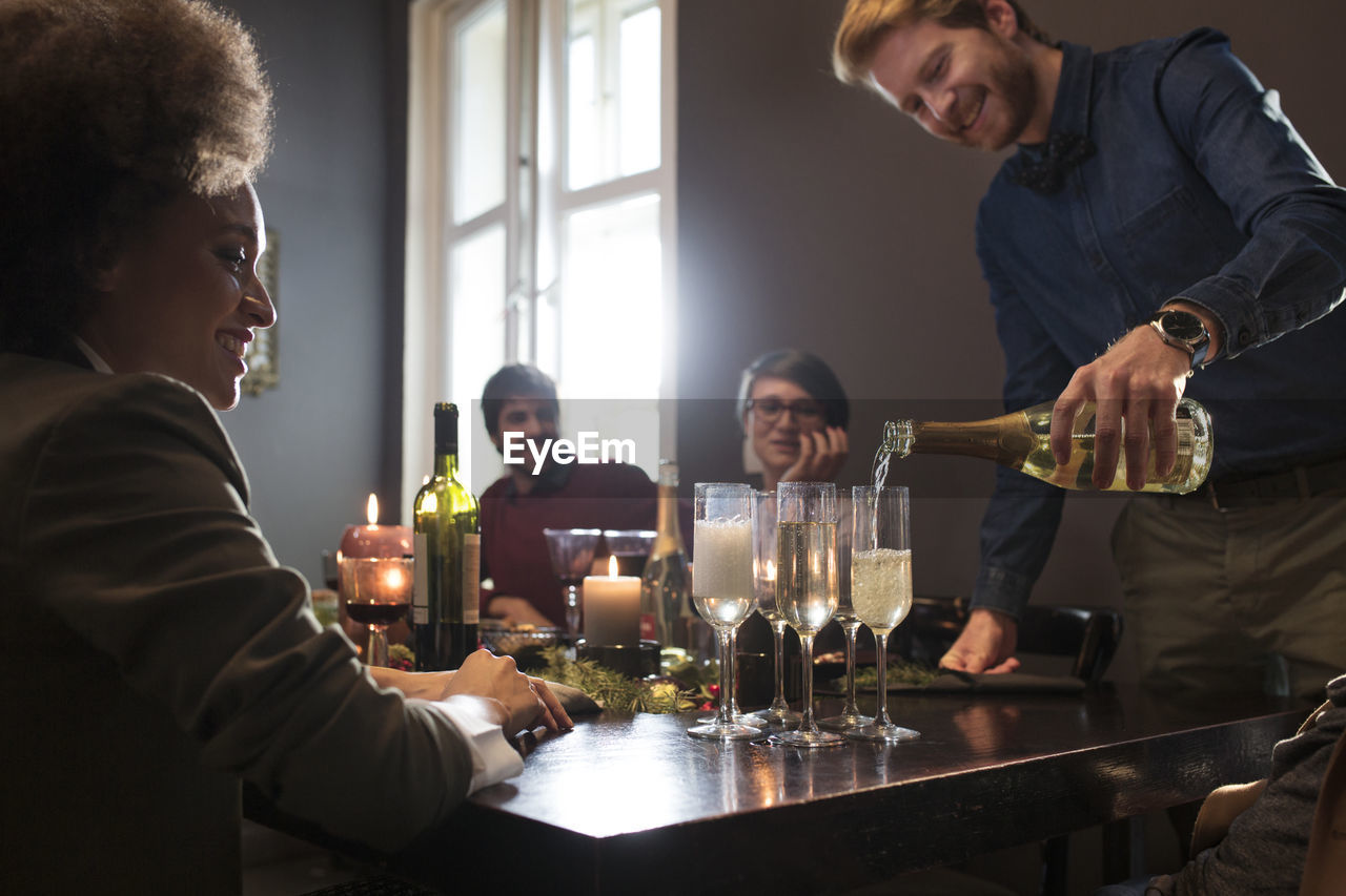 Man pouring champagne in glasses for friends during christmas party