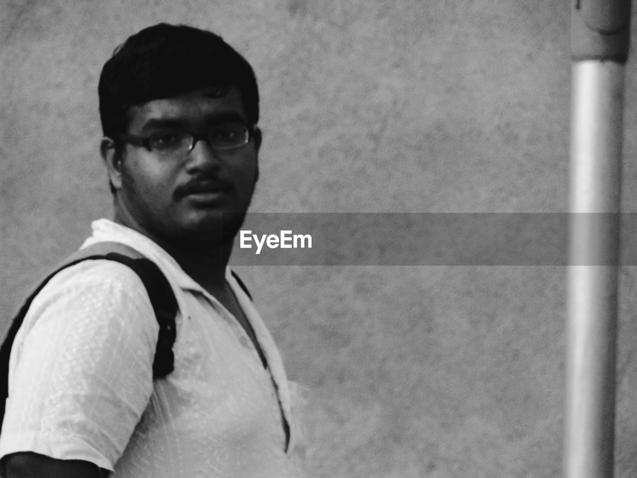 PORTRAIT OF YOUNG MAN WEARING EYEGLASSES STANDING AGAINST WALL
