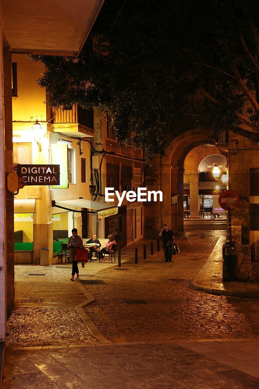 MAN WALKING IN ILLUMINATED CITY AT NIGHT