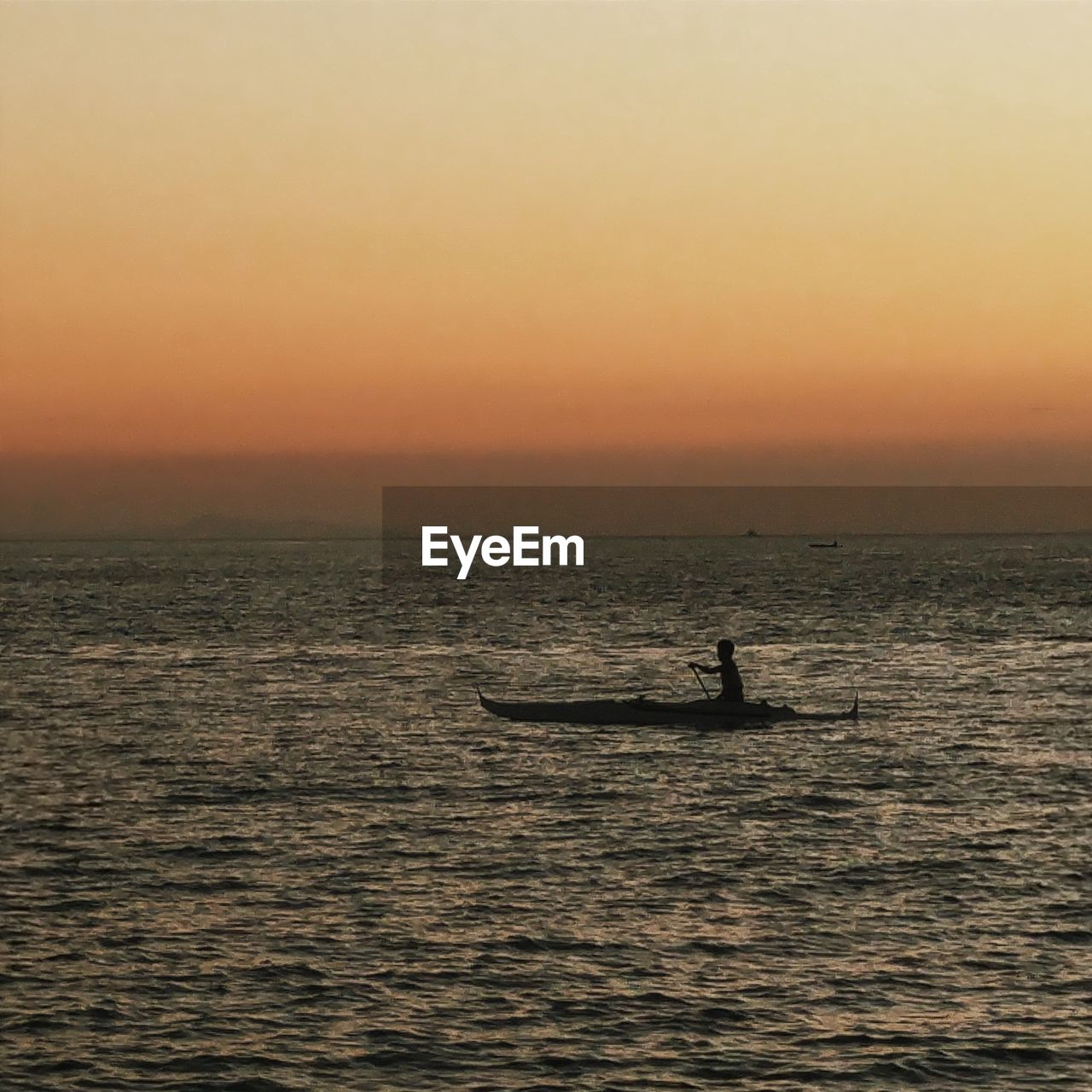 Silhouette man rowing boat in sea during sunset