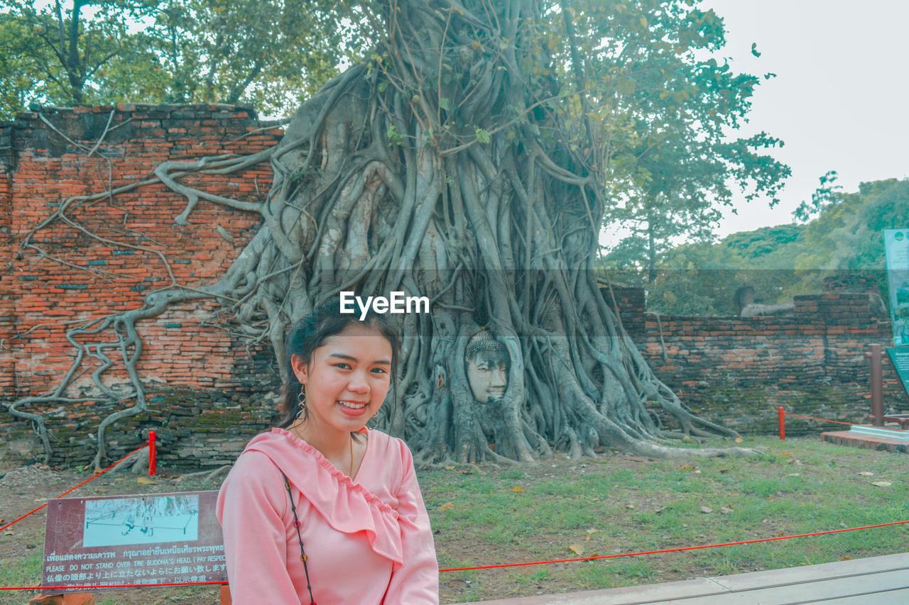 Portrait of smiling young woman against tree