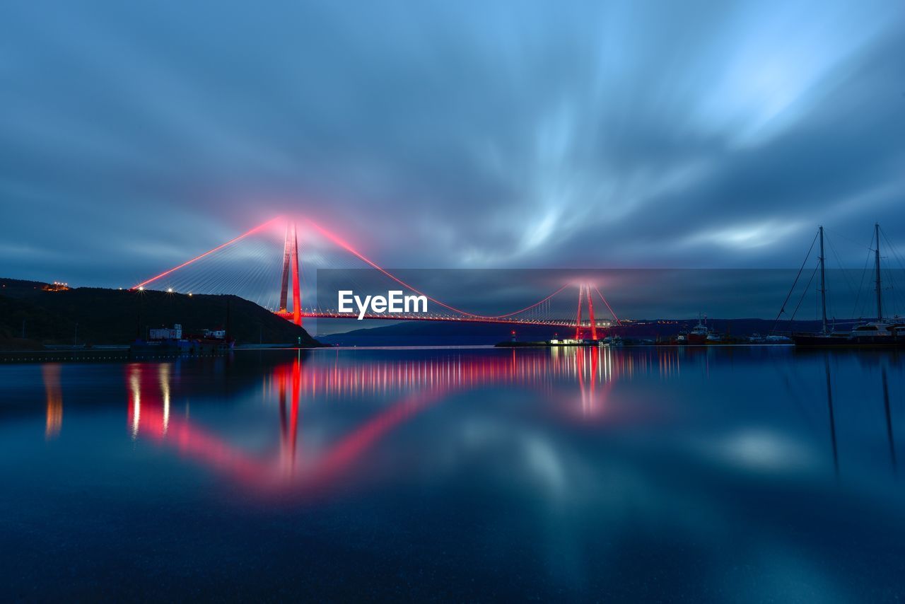 Illuminated suspension bridge over sea against sky