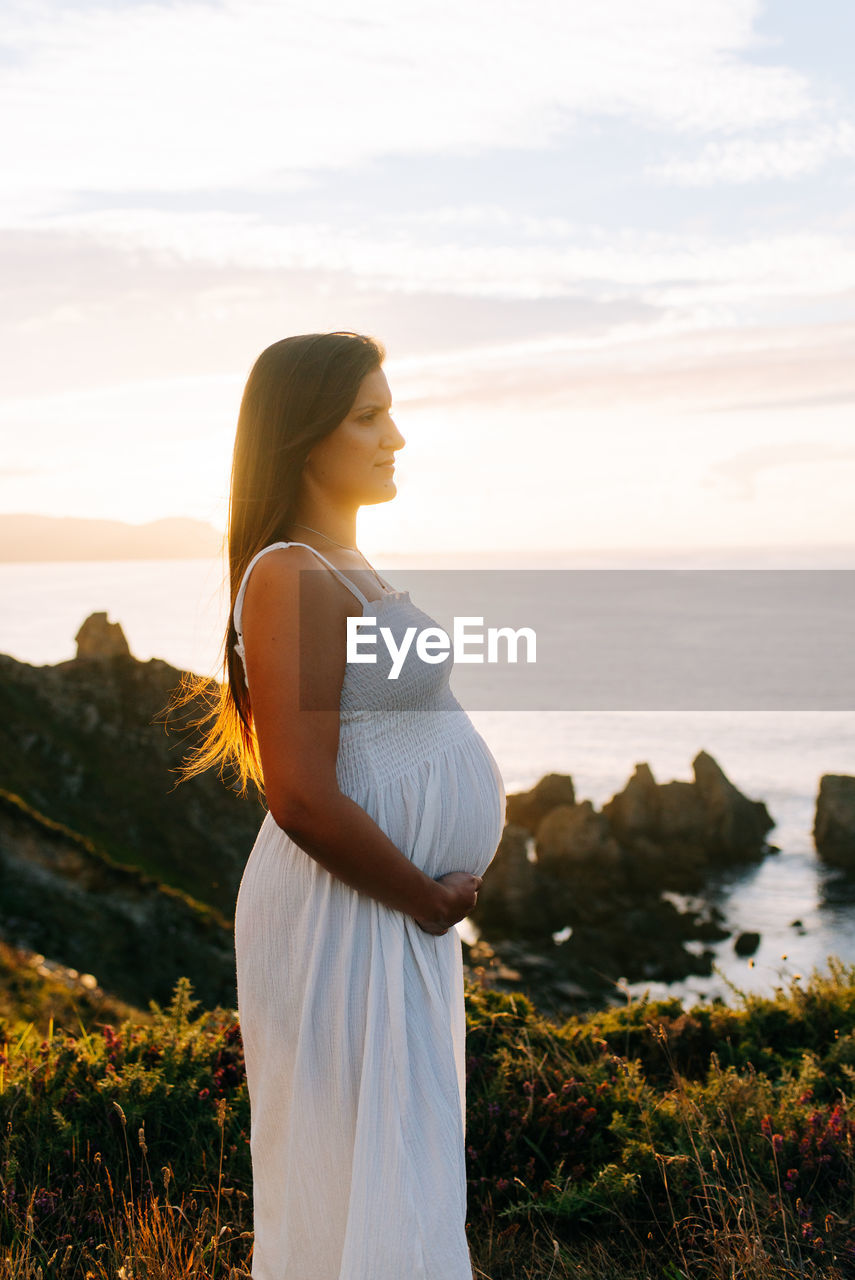 Woman standing by sea against sky during sunset