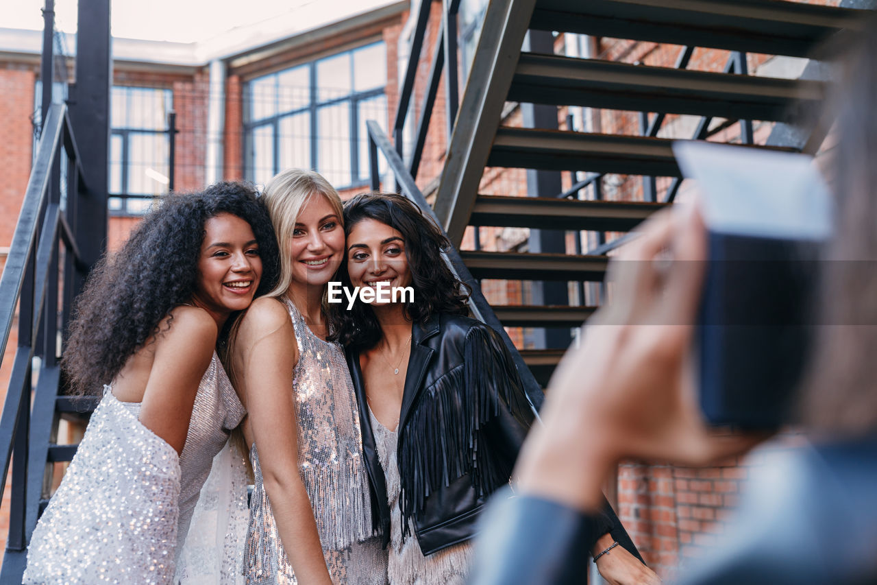 Cropped image of woman photographing happy female friends standing on staircase