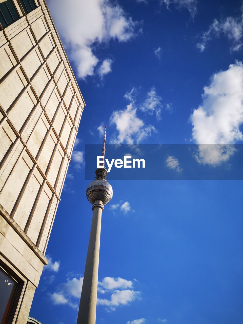 Low angle view of communications tower against blue sky during sunny day in city