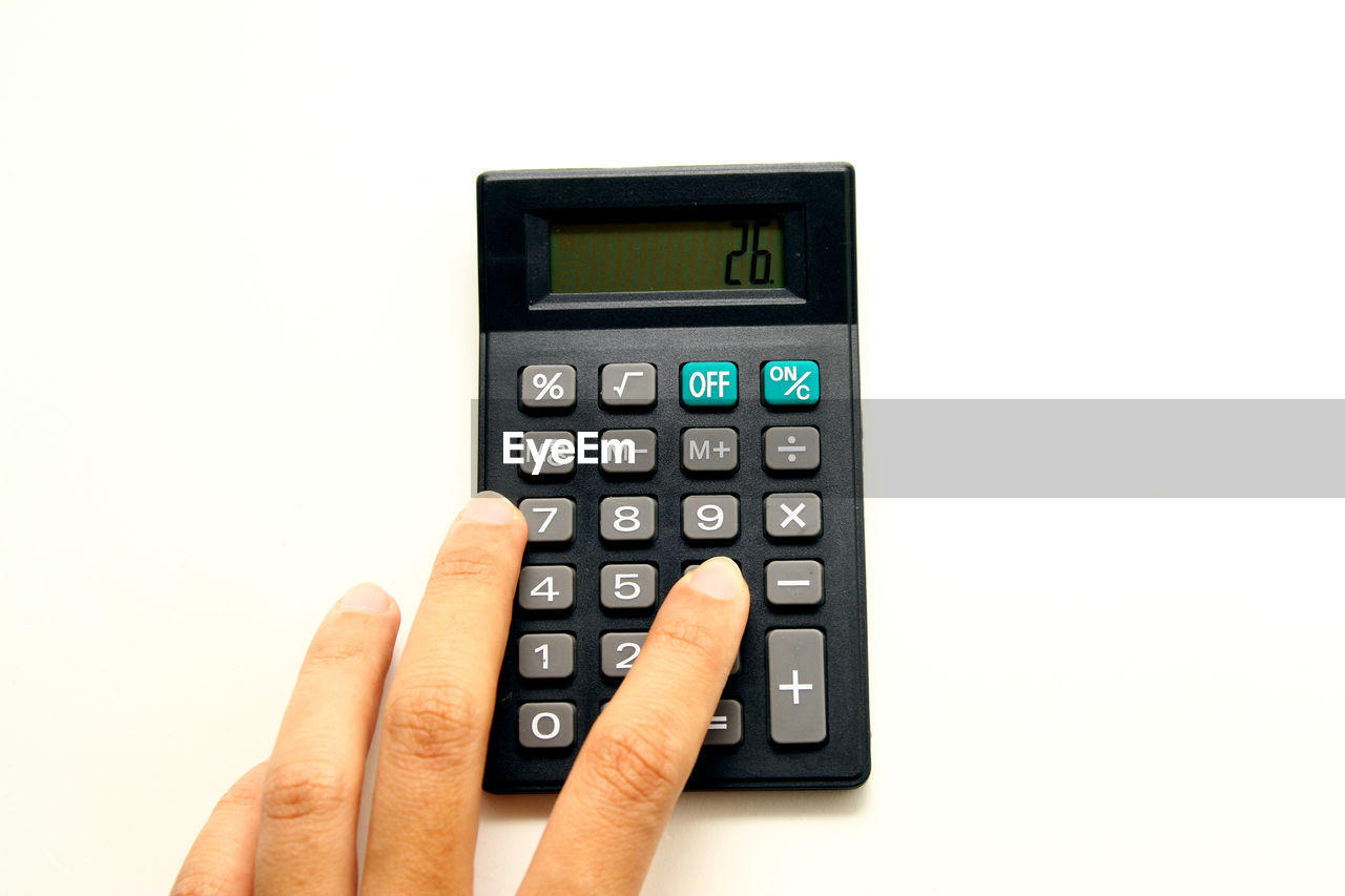 Close-up of hand using calculator against white background