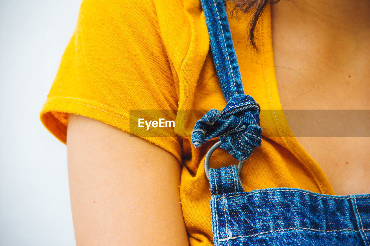 Cropped image of woman wearing bib overalls against wall