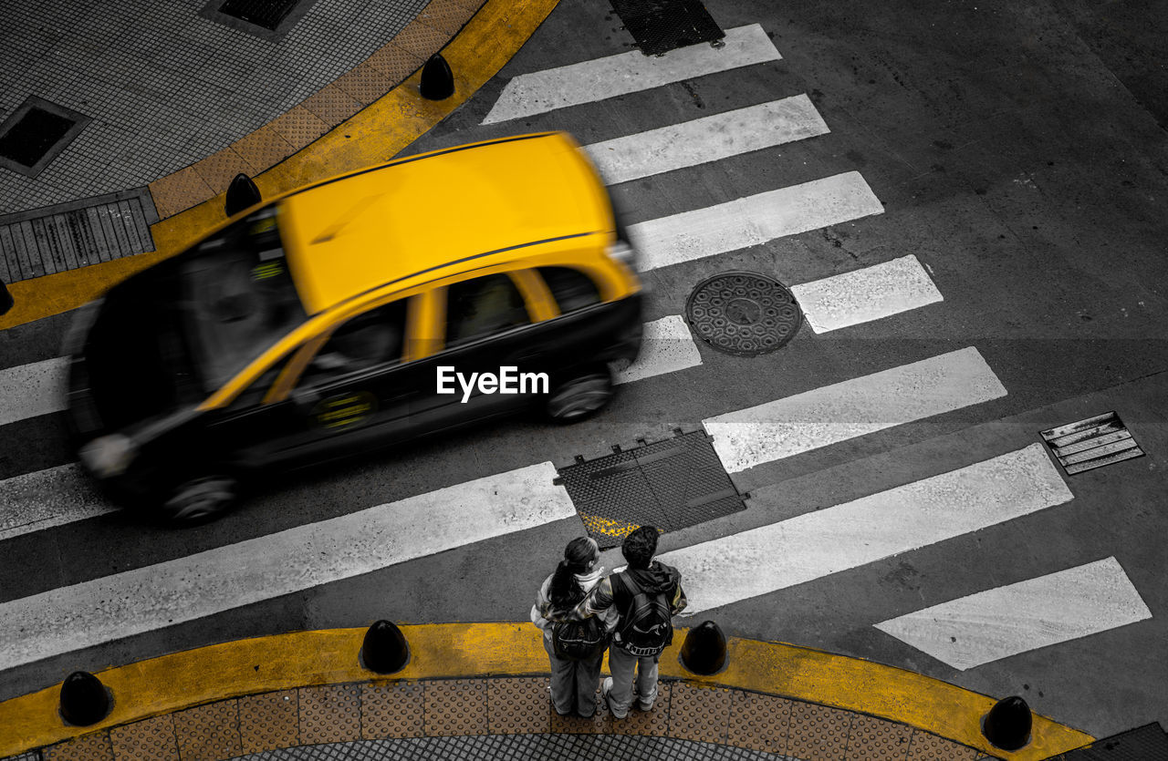 transportation, road marking, crosswalk, zebra crossing, road, marking, city, yellow, crossing, symbol, high angle view, street, sign, mode of transportation, yellow taxi, architecture, taxi, city life, car, city street, motor vehicle, black, land vehicle, pedestrian crossing, walking, on the move, motion, adult, day, men, public transportation, protection, traffic, outdoors, travel, crossroad, vehicle