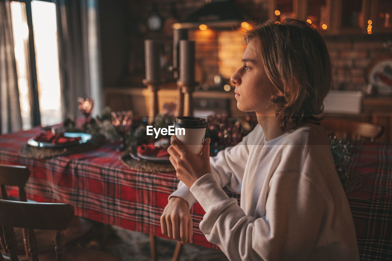 Portrait of candid authentic smiling handsome boy teenager using mobile phone at xmas home interior