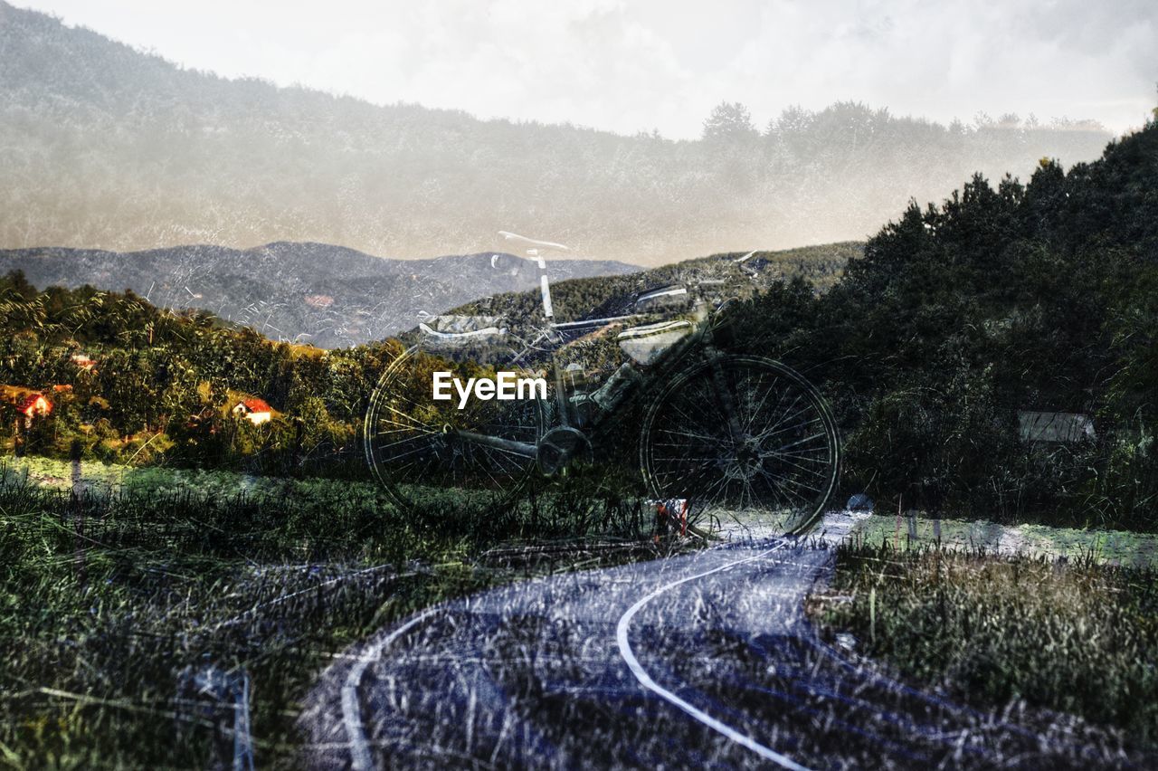 Digital composite image of bicycle on road against landscape and sky