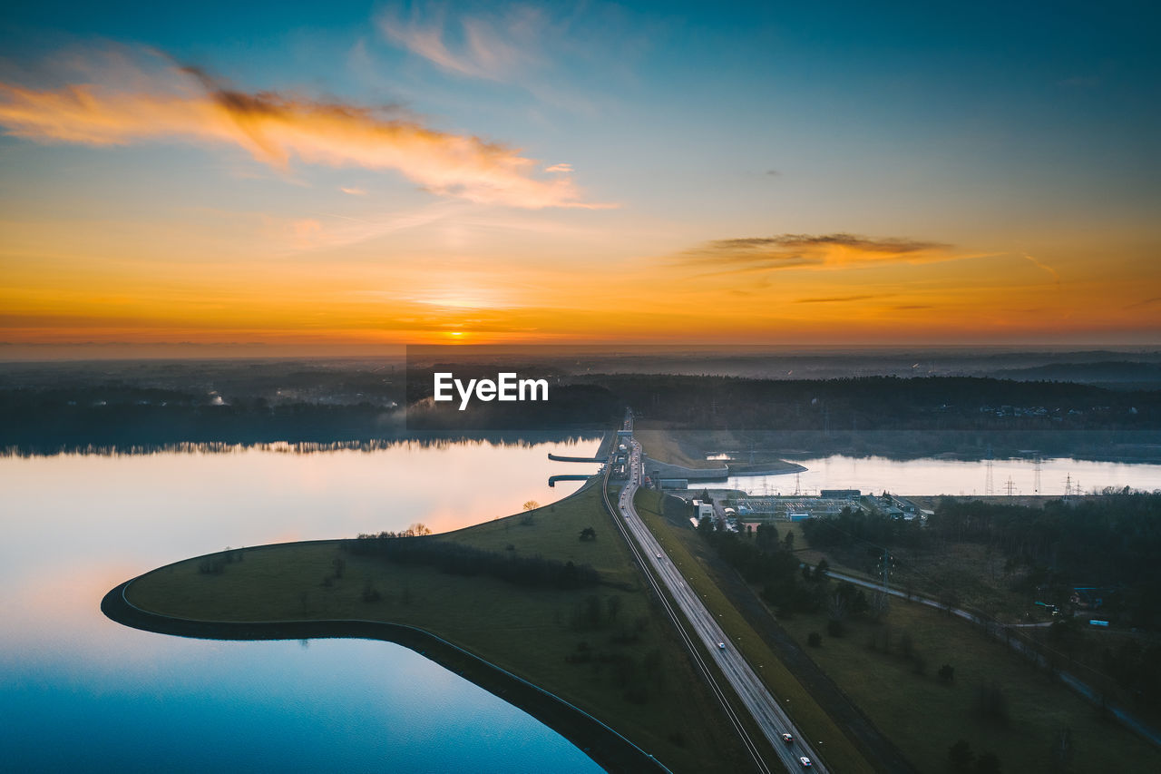 Scenic view of landscape and dam against sky during sunset