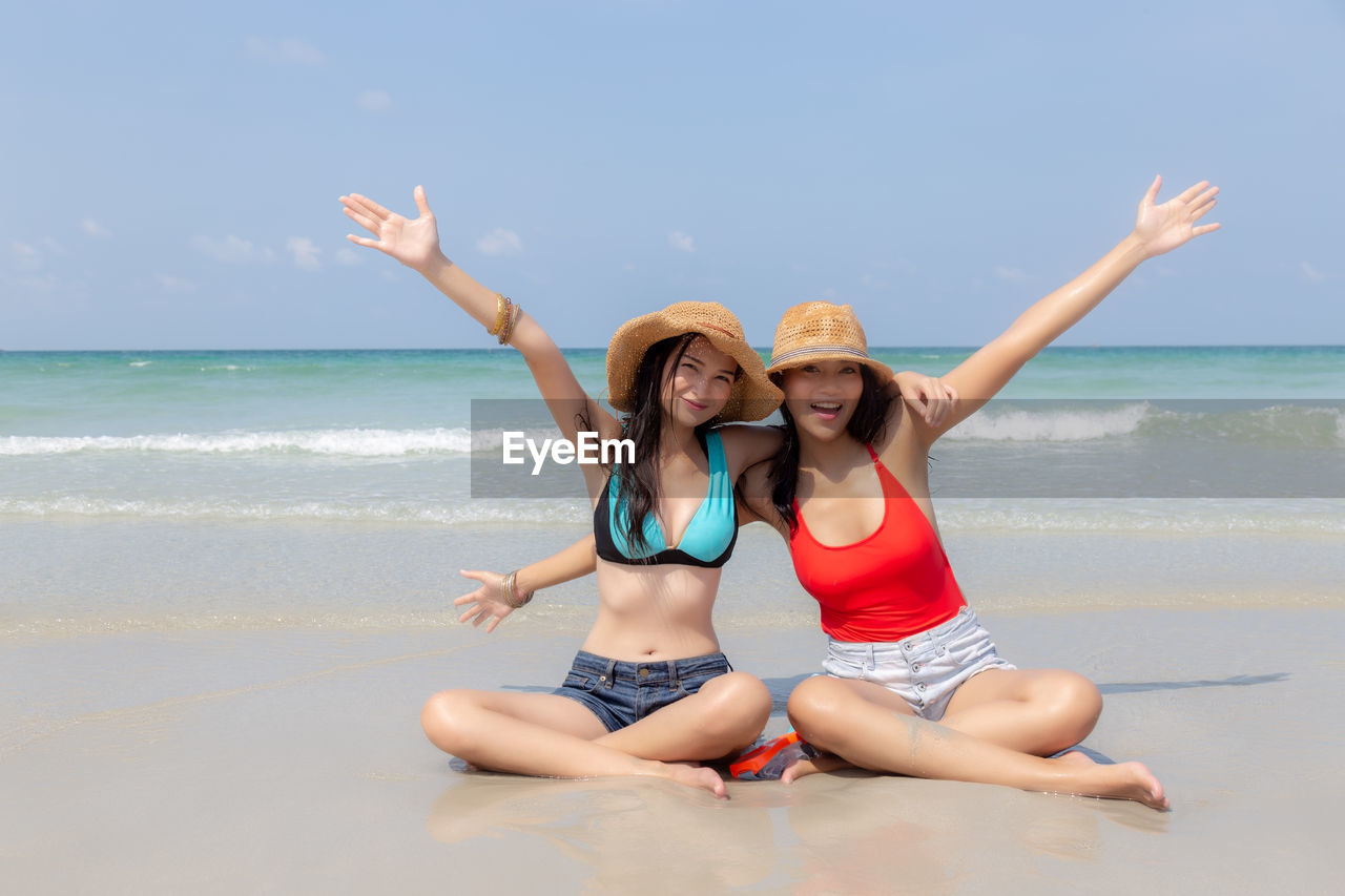 Portrait of smiling young friends with arms raised sitting on beach