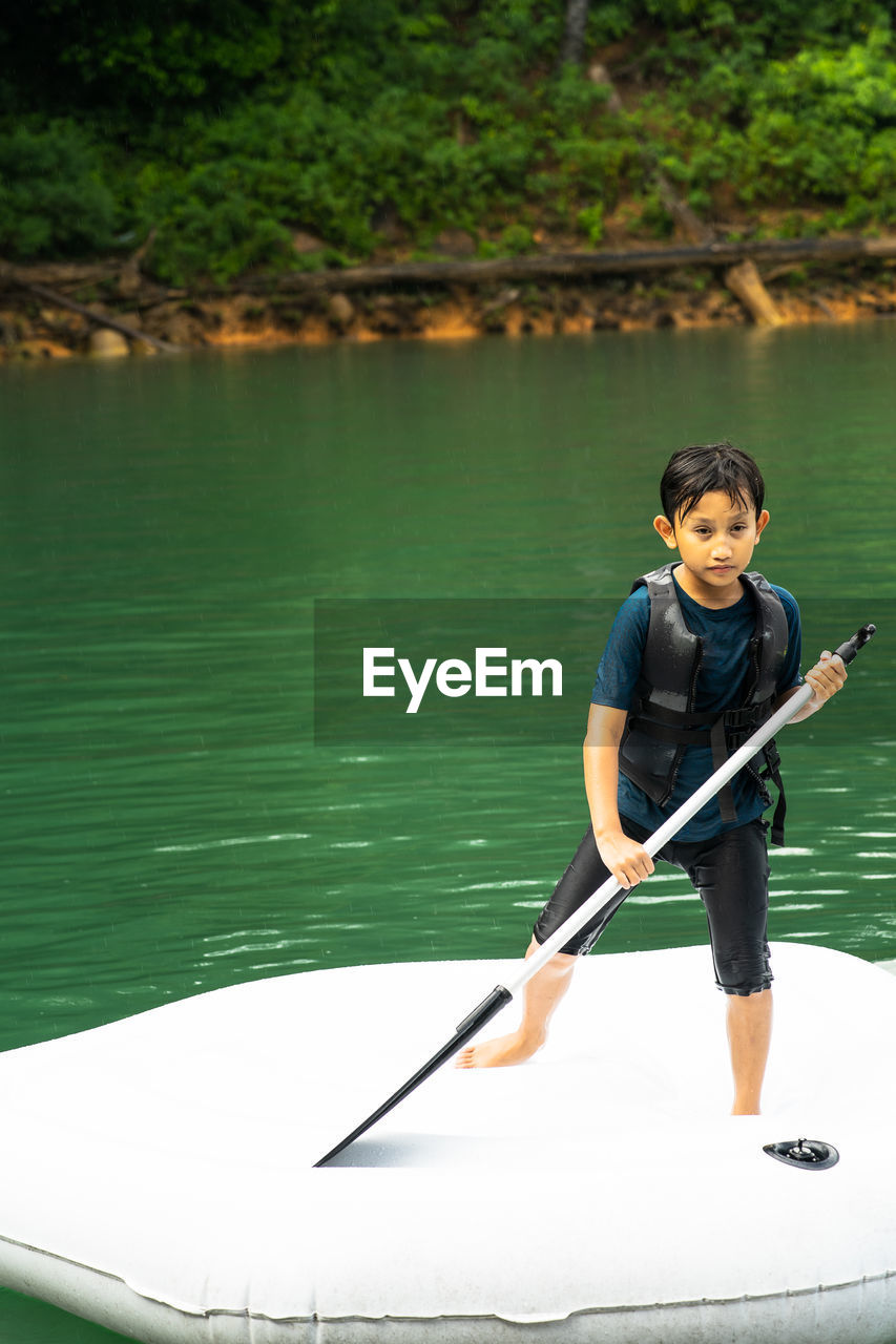 Young boy wearing life jackets paddling on an inflatable boat in kenyir lake, malaysia.