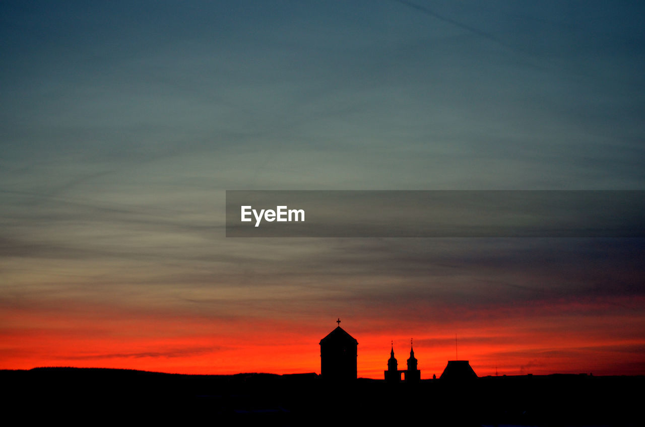 Silhouette buildings against cloudy sky during sunset