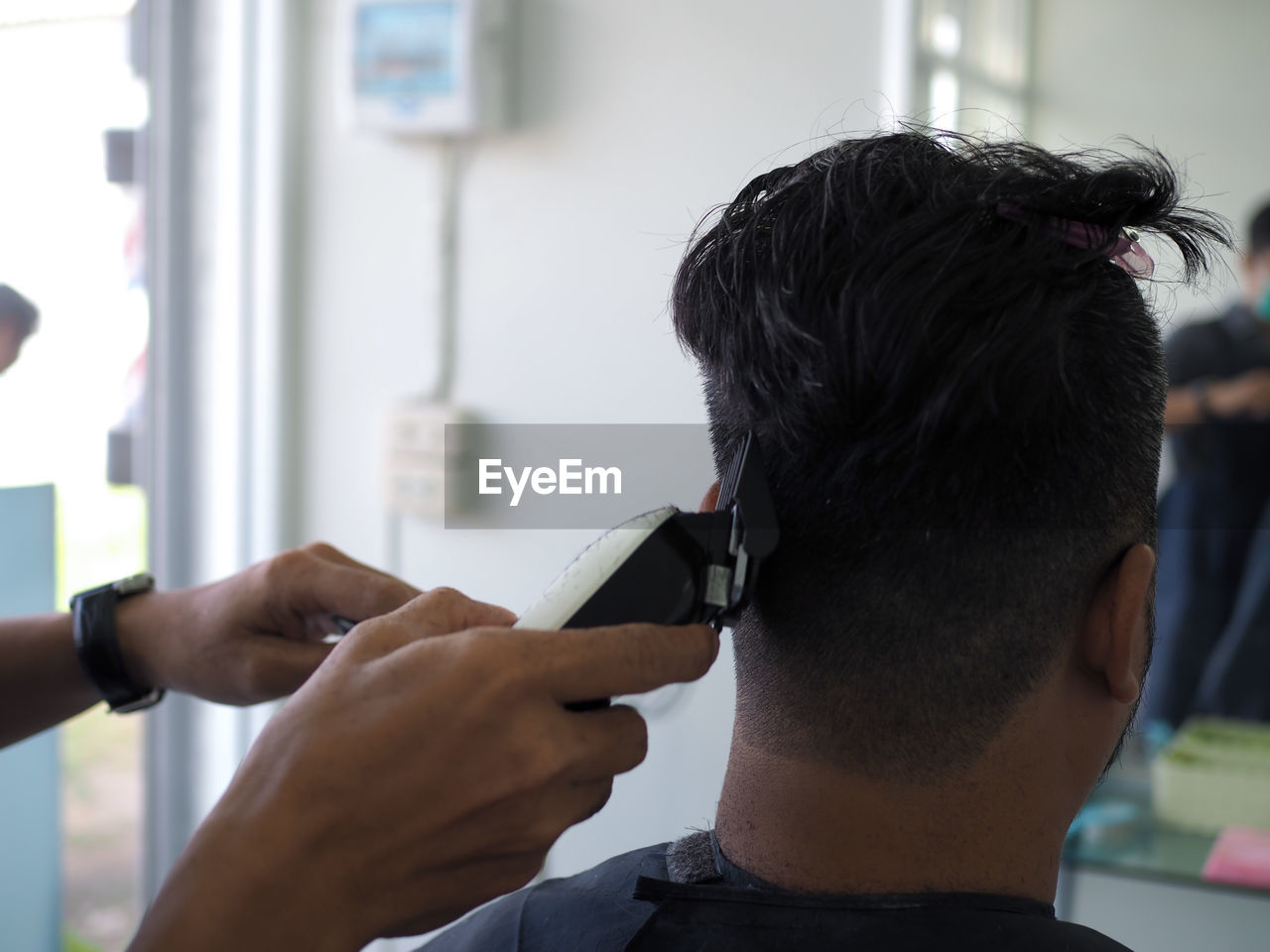 Cropped hands of barber cutting male customer hair in shop