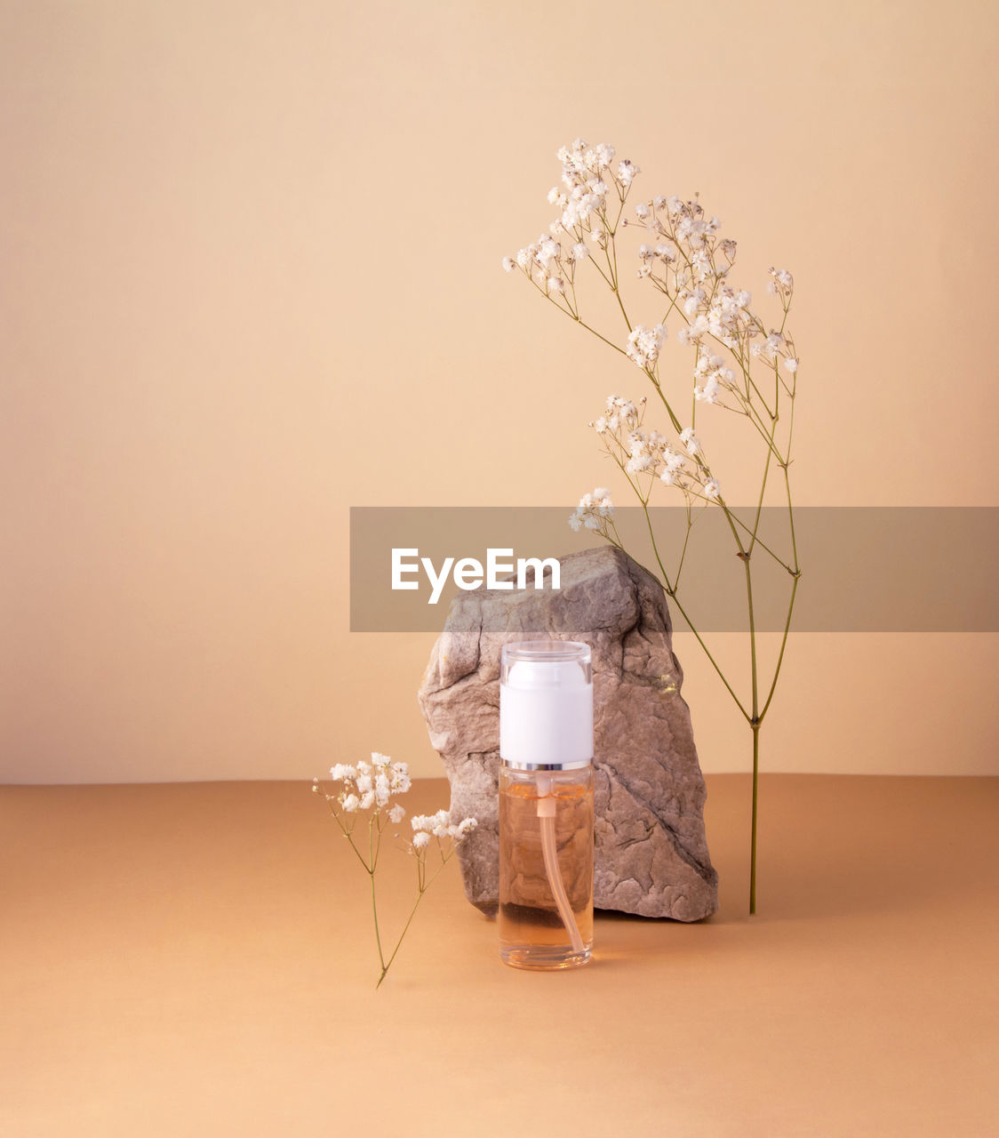 Cosmetic bottle with gel or other cosmetic product, stones, dried plant flowers on beige background.