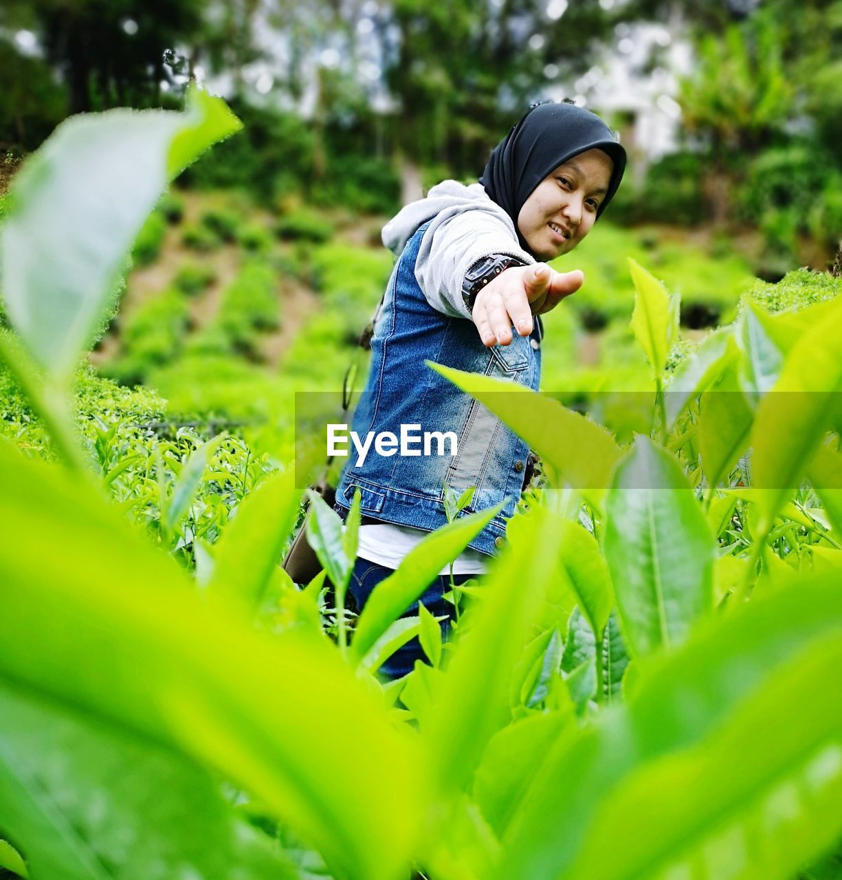 Portrait of woman pointing at camera while standing by plants
