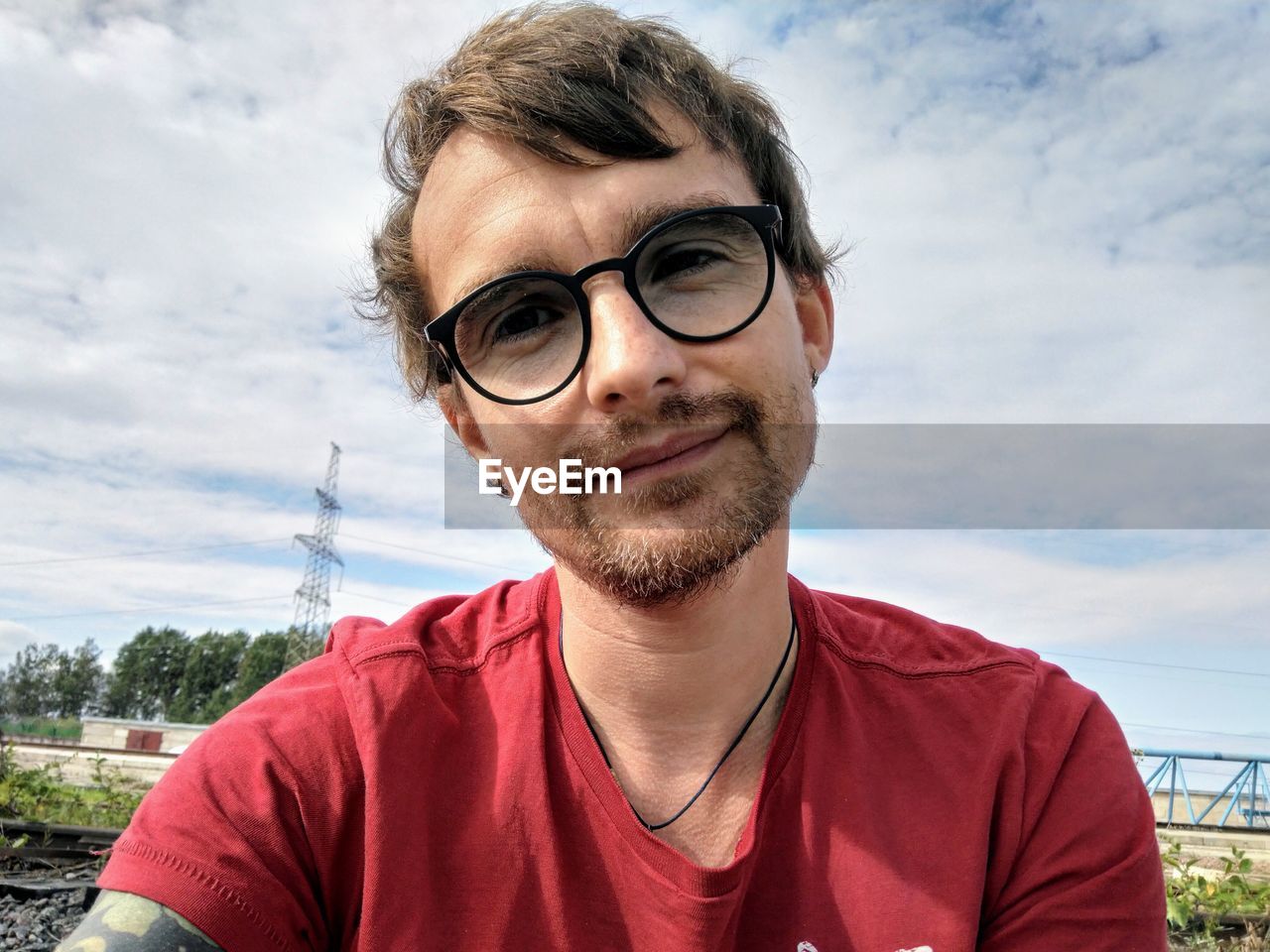 Portrait of young man with eyeglasses against sky