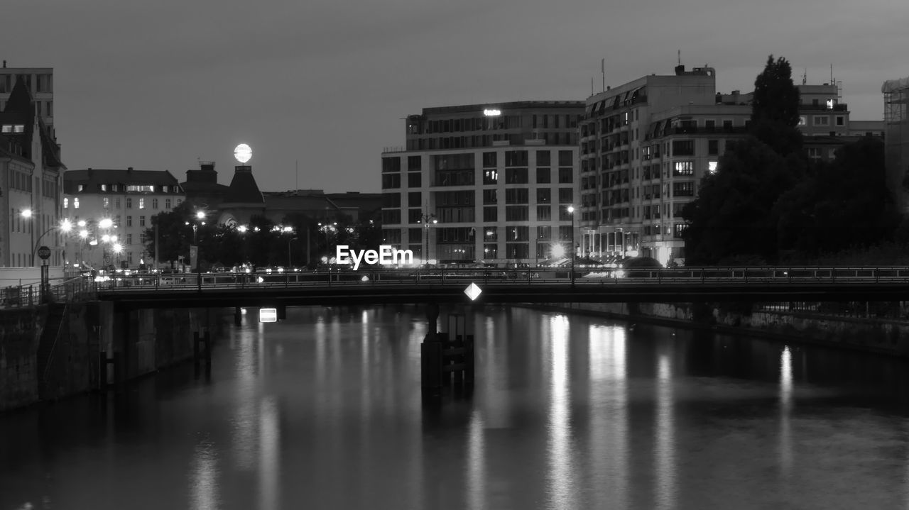 ILLUMINATED BUILDINGS BY RIVER AGAINST SKY