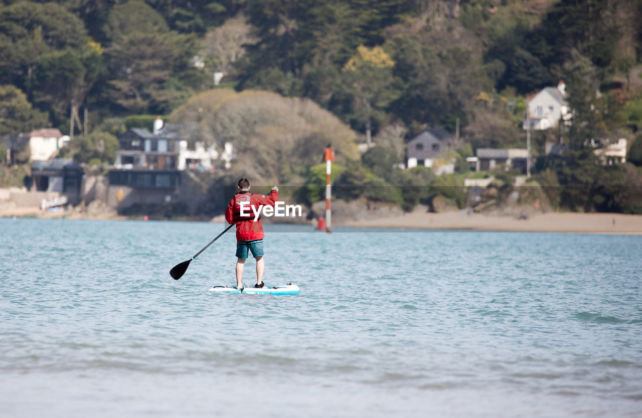 MAN STANDING IN SEA AGAINST TREES