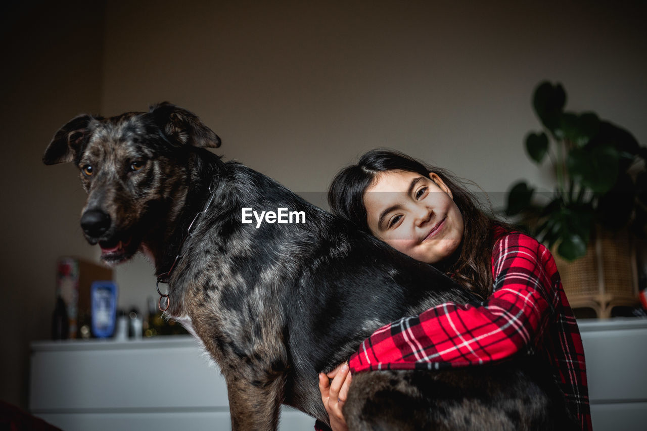 Smiling girl in checked pajama hugs her grey dog