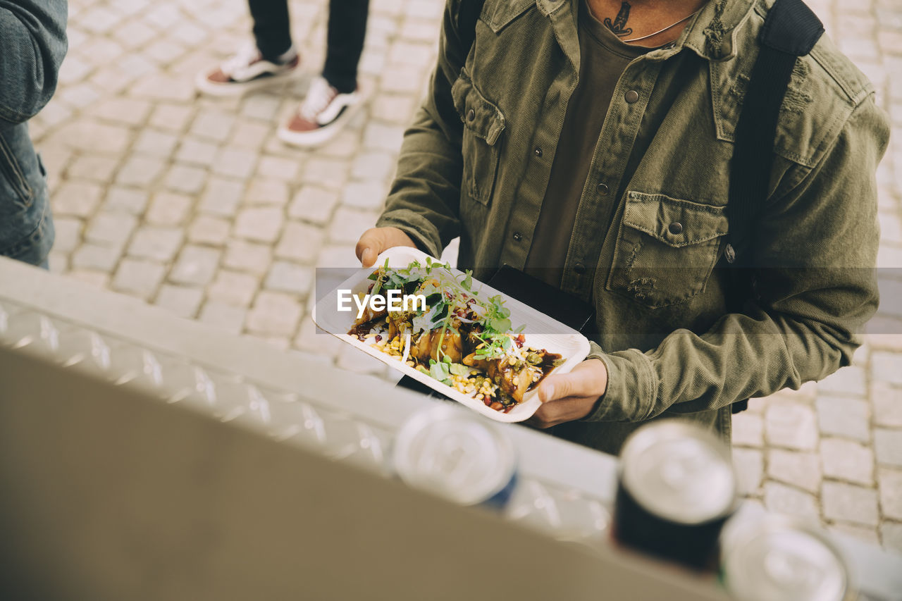 Midsection of male customer holding food plate by commercial land vehicle