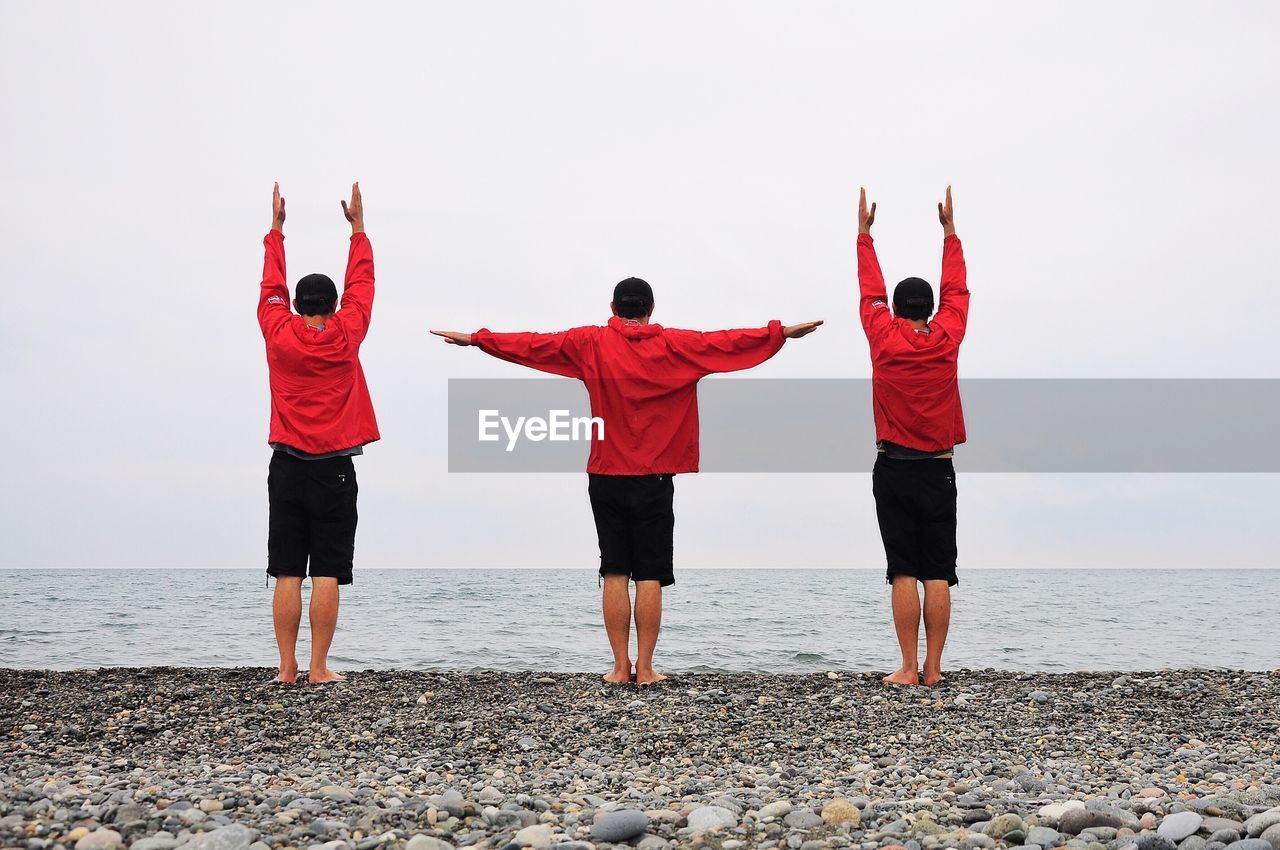 Rear view of friends exercising at beach against sky