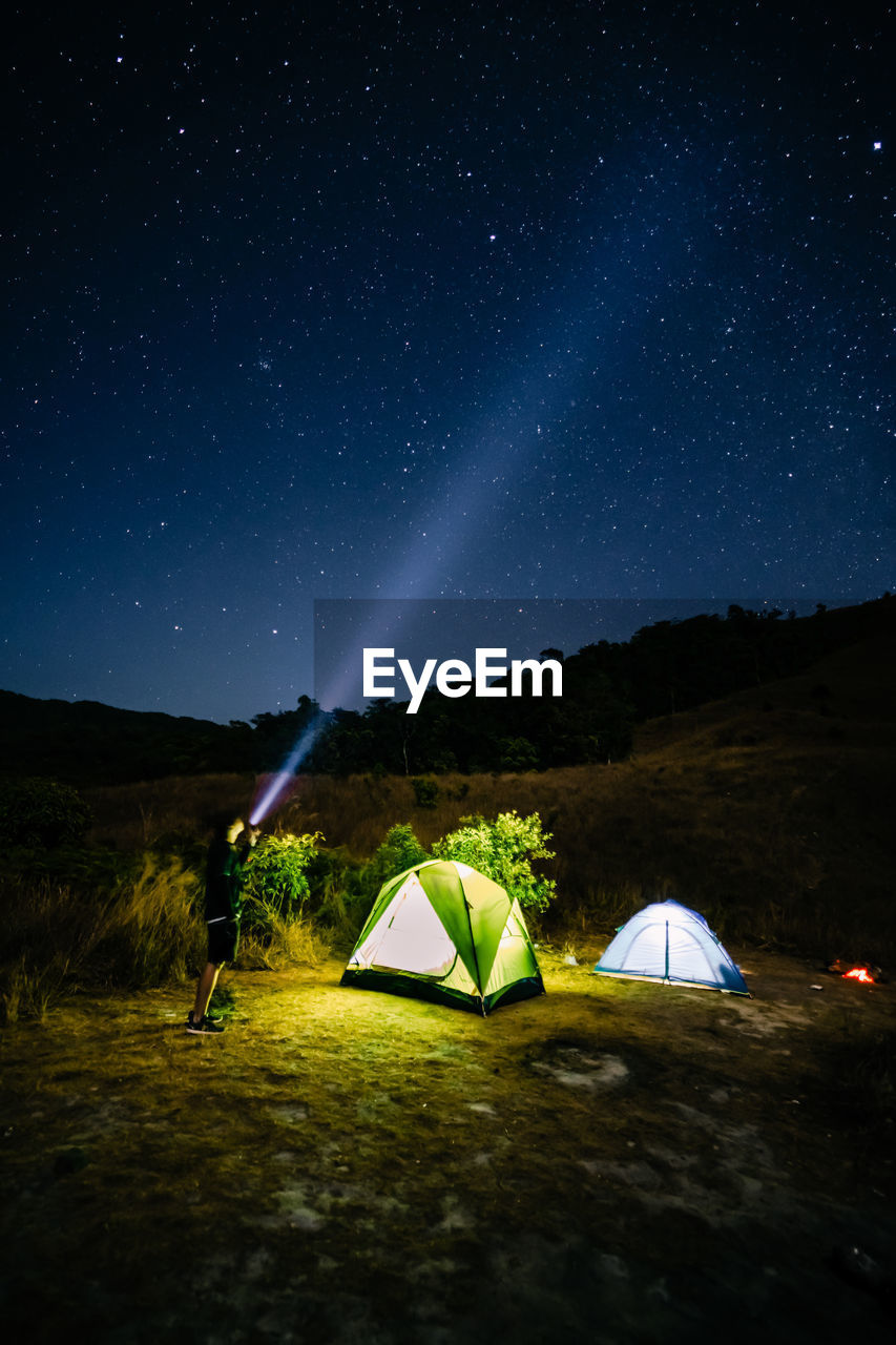 Tent on field against sky at night with photographer 