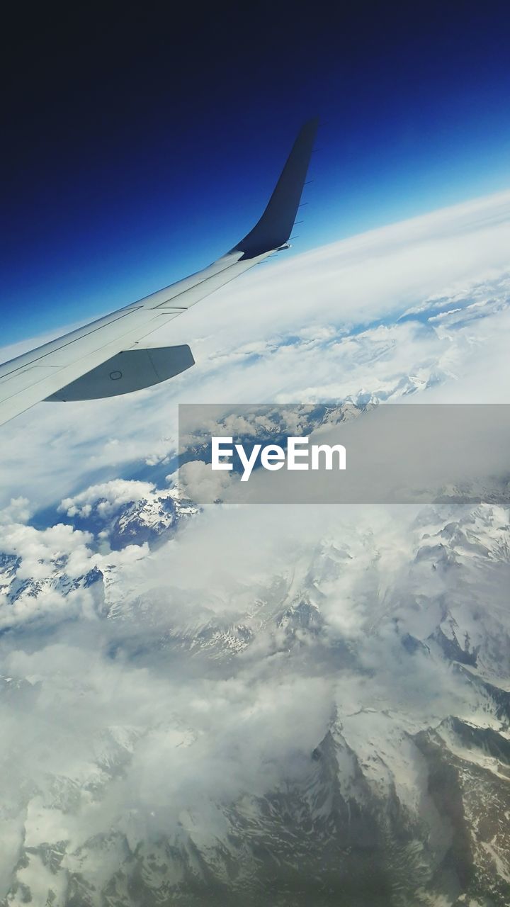 CROPPED IMAGE OF AIRPLANE FLYING OVER MOUNTAINS