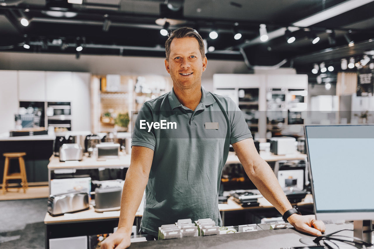 Portrait of smiling mature salesman standing at counter in electronics store