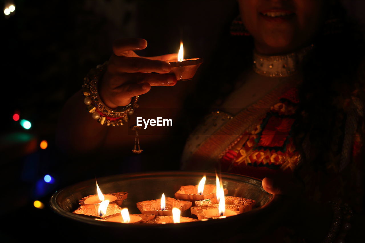 Midsection of woman holding lit diyas in plate