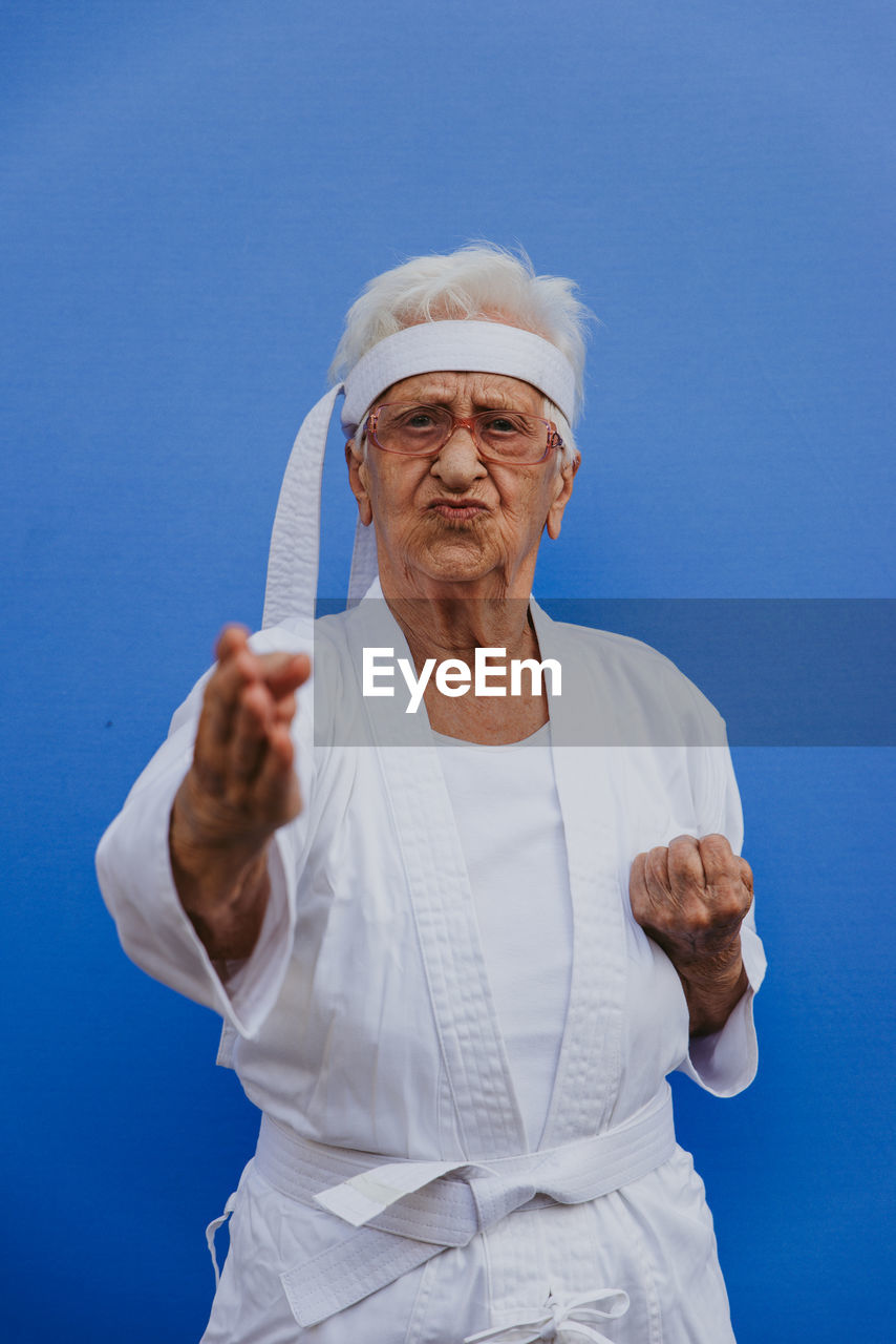 Portrait of senior woman doing karate against blue background