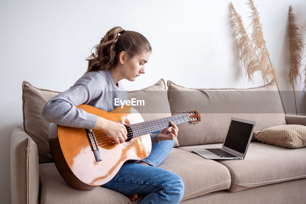 Side view of girl playing guitar at home