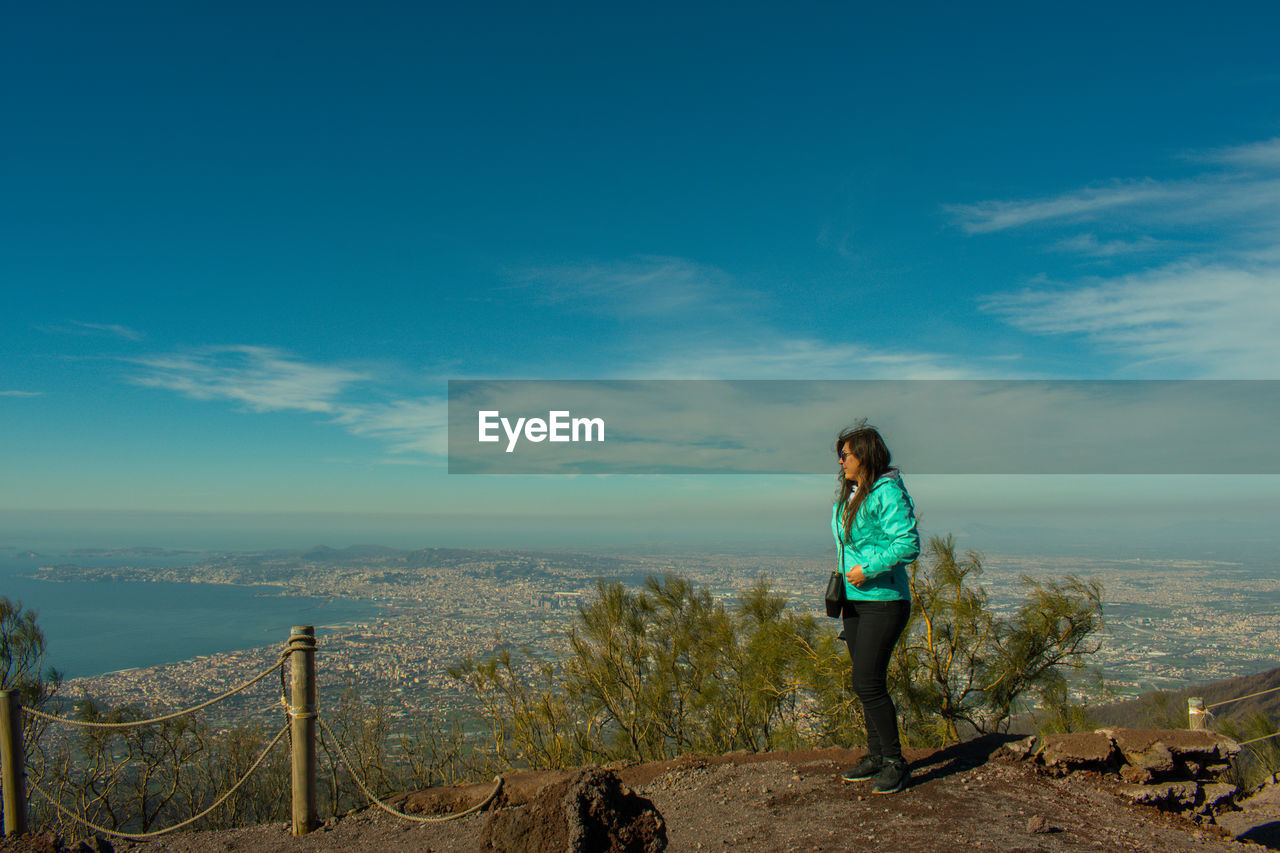 Side view of mid adult woman standing on mountain against blue sky